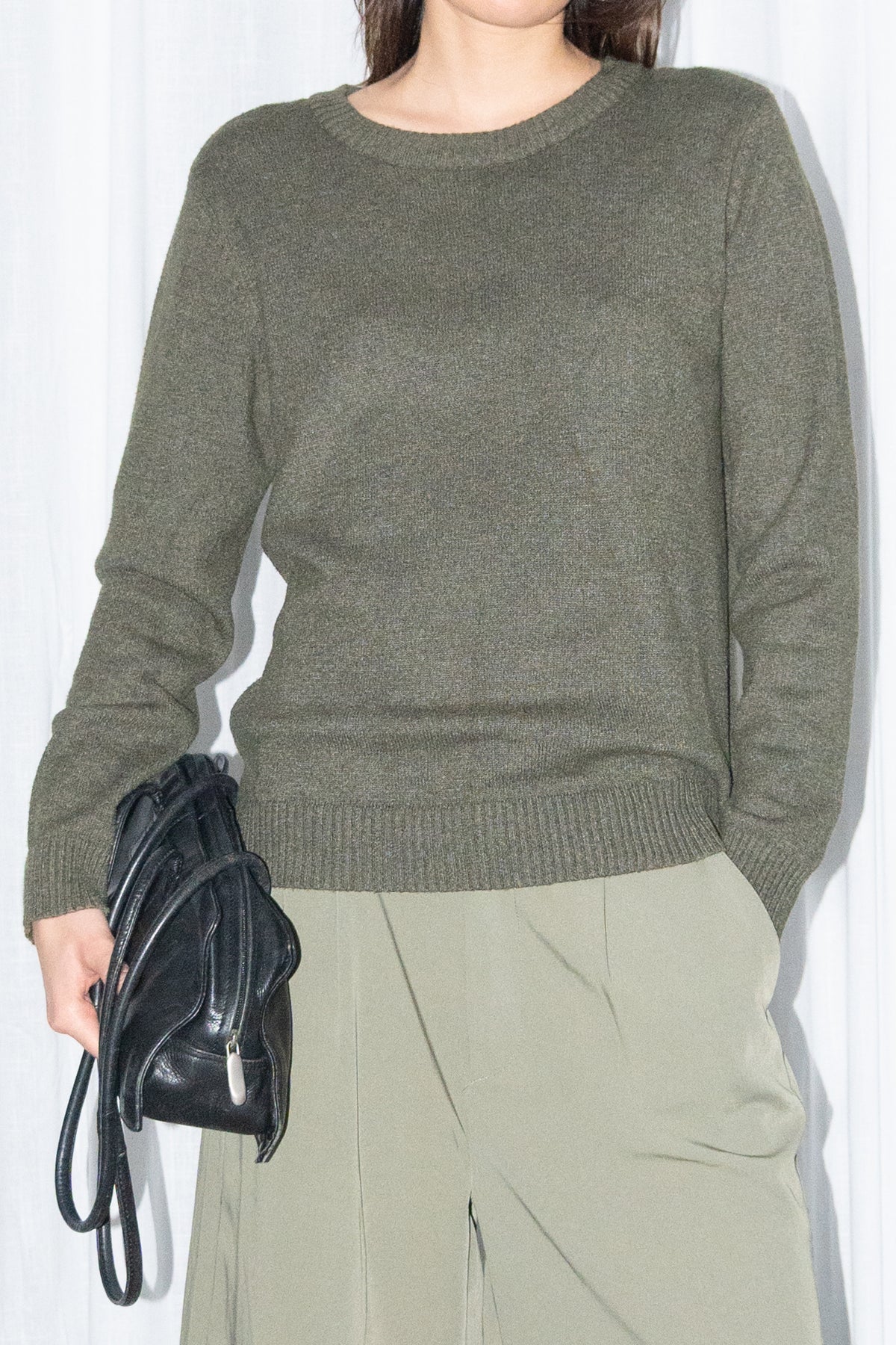 Close-up of a dark olive green crew-neck knit sweater with khaki green pleated Bermuda shorts