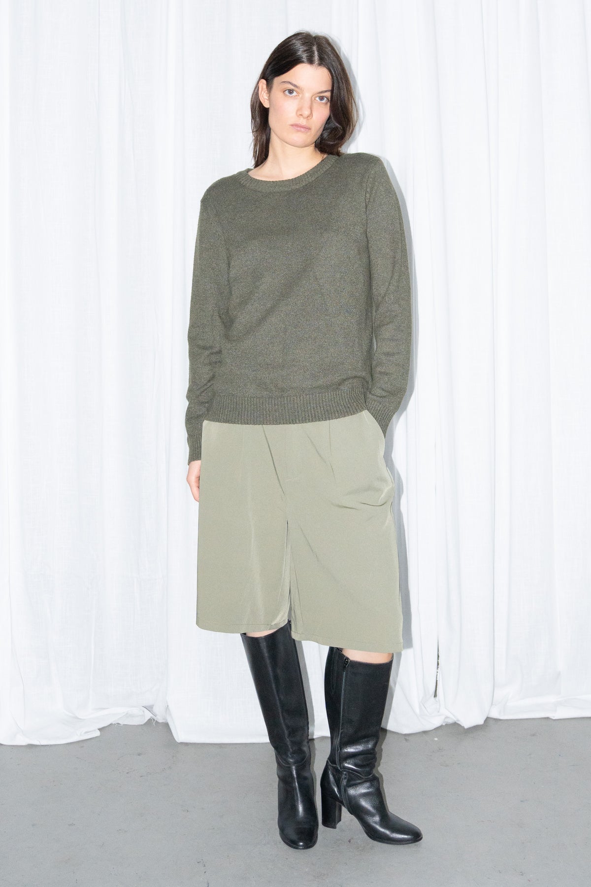 Front view of a dark olive green crew-neck knit sweater with khaki green tailored Bermuda shorts