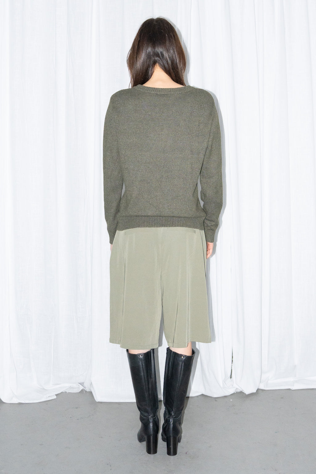 Back view of a dark olive green crew-neck knit sweater with khaki green Bermuda shorts