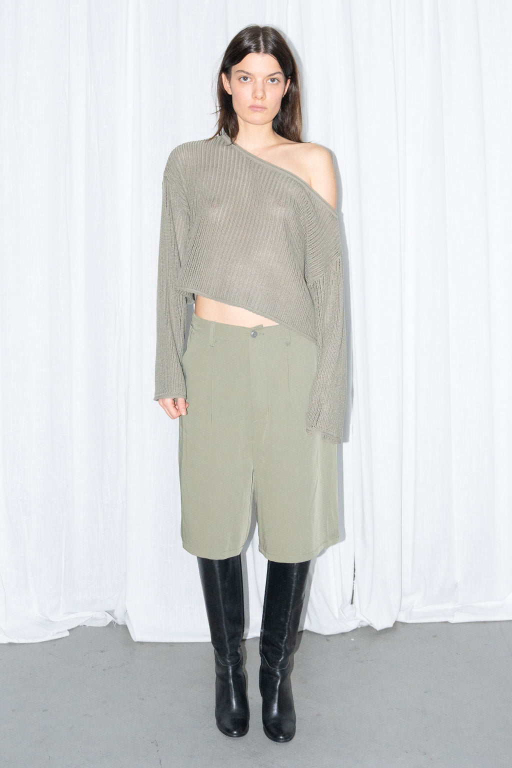Model wearing an olive off-shoulder chunky knit sweater with khaki green tailored Bermuda shorts and black knee boots