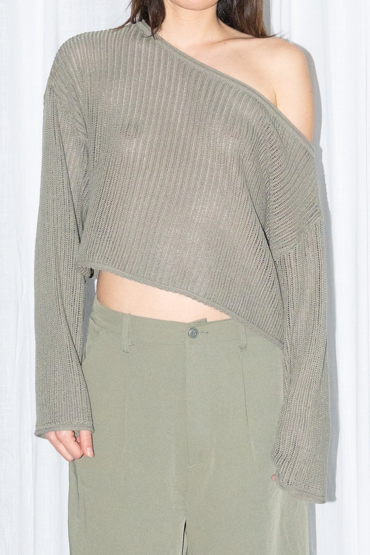 Close-up of an olive off-shoulder ribbed knit sweater with khaki green pleated Bermuda shorts