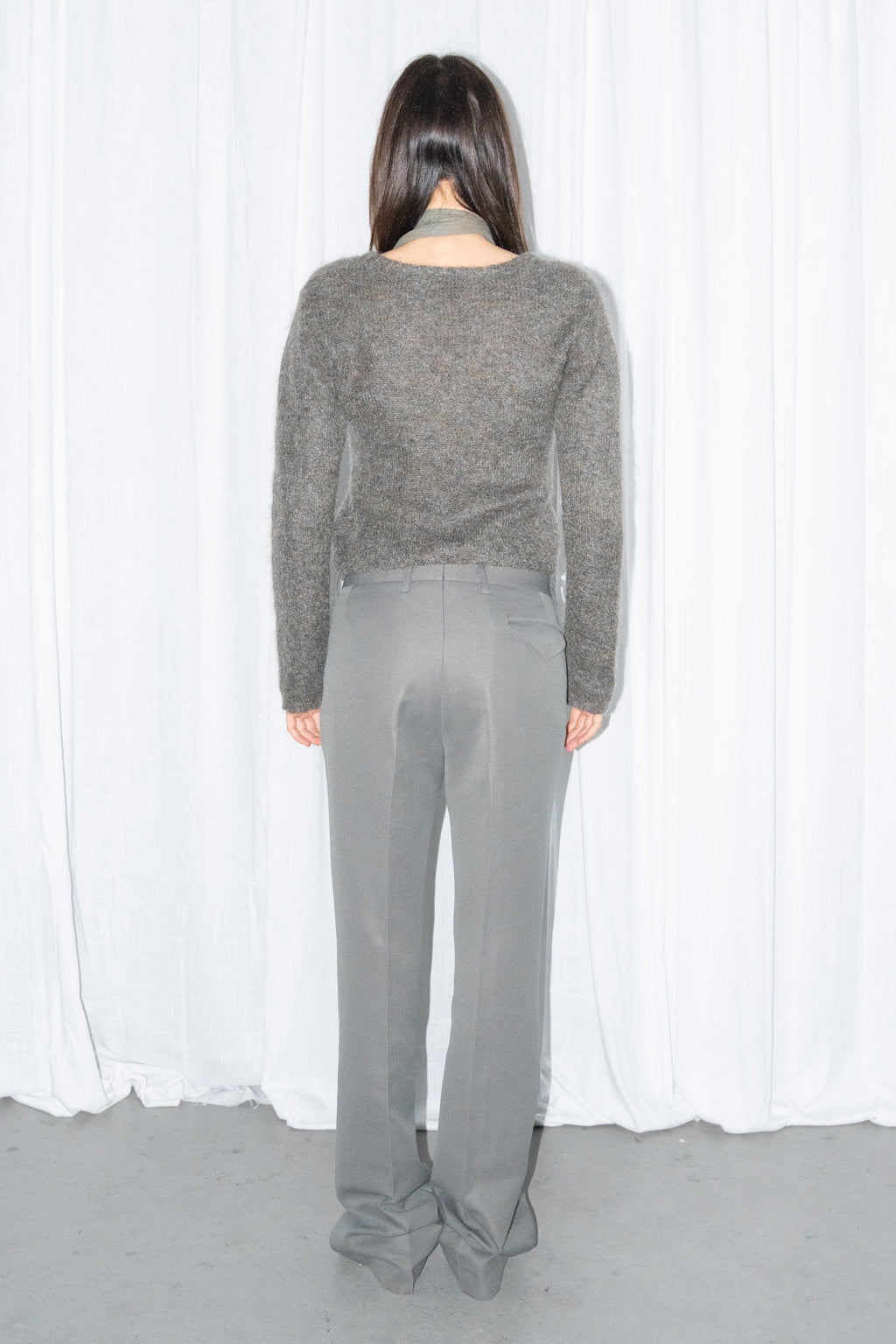 Back view of a grey fluffy cropped mohair knit sweater with grey wide-leg trousers and a grey scarf