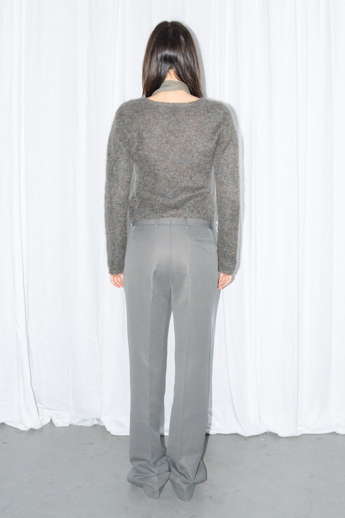 Back view of a grey fluffy cropped mohair knit sweater with grey wide-leg trousers and a grey scarf