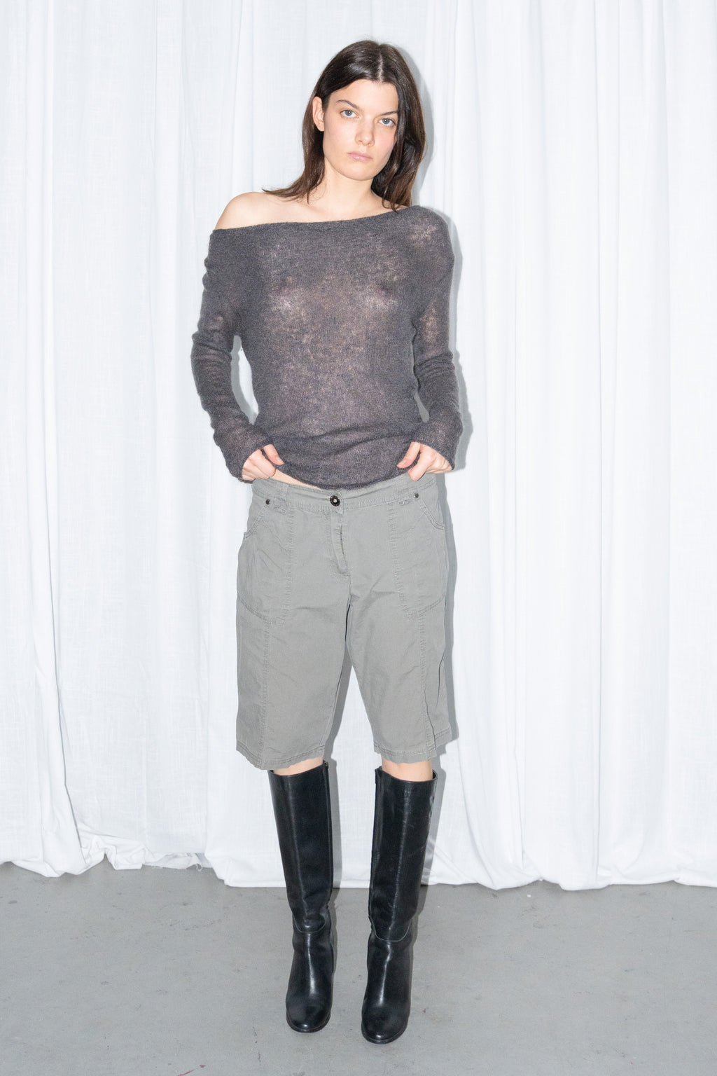 Model wearing a charcoal brown off-shoulder fitted top with khaki green cargo Bermuda shorts and black knee boots