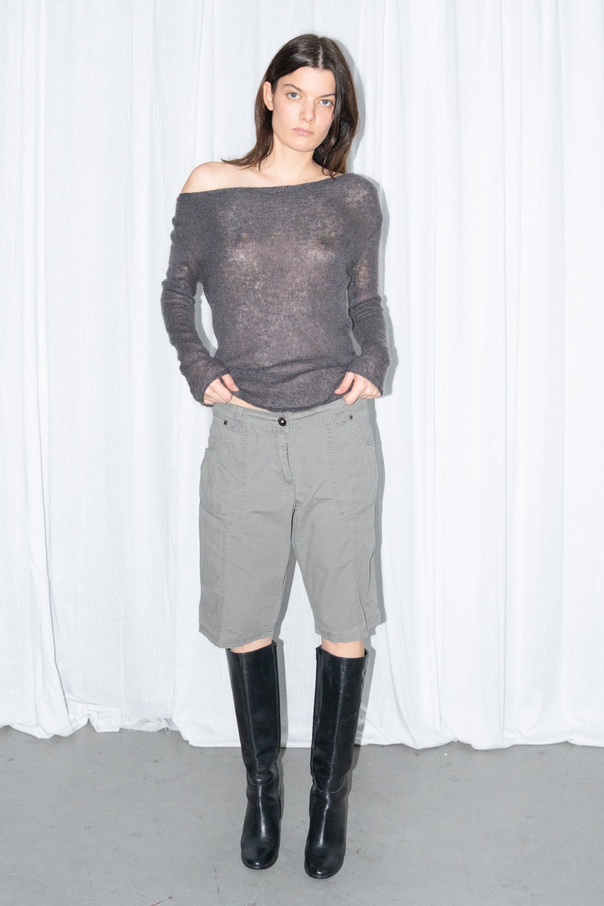 Model wearing a charcoal brown off-shoulder fitted top with khaki green cargo Bermuda shorts and black knee boots
