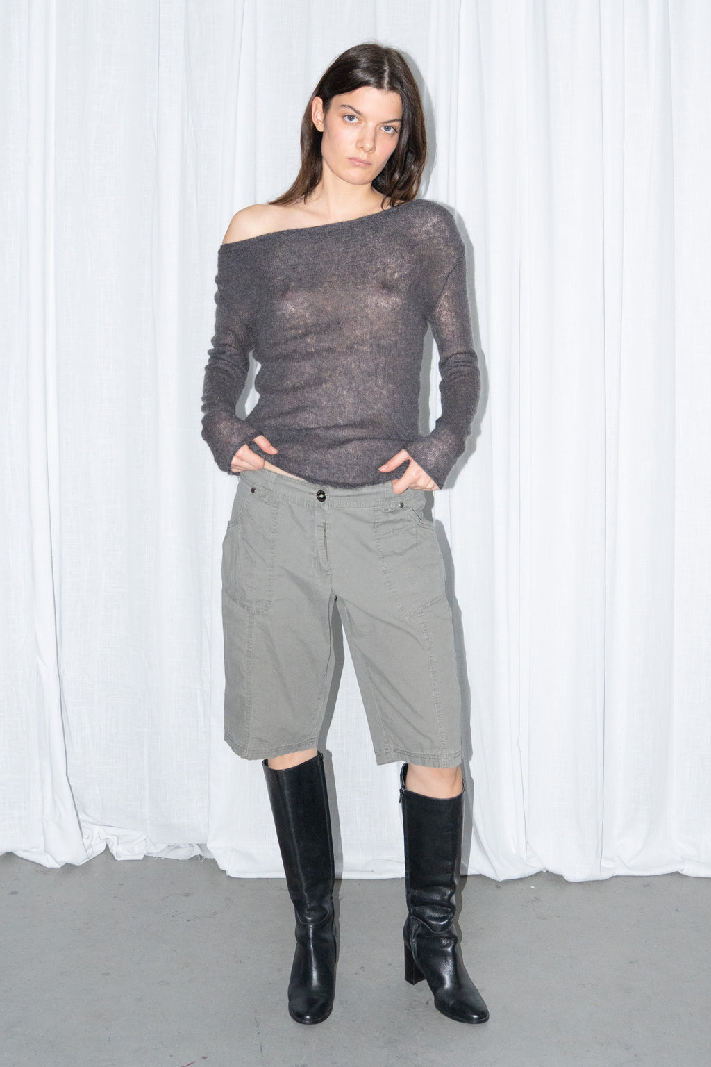 Model posing in a charcoal brown off-shoulder fitted top with khaki green cargo Bermuda shorts and black knee boots