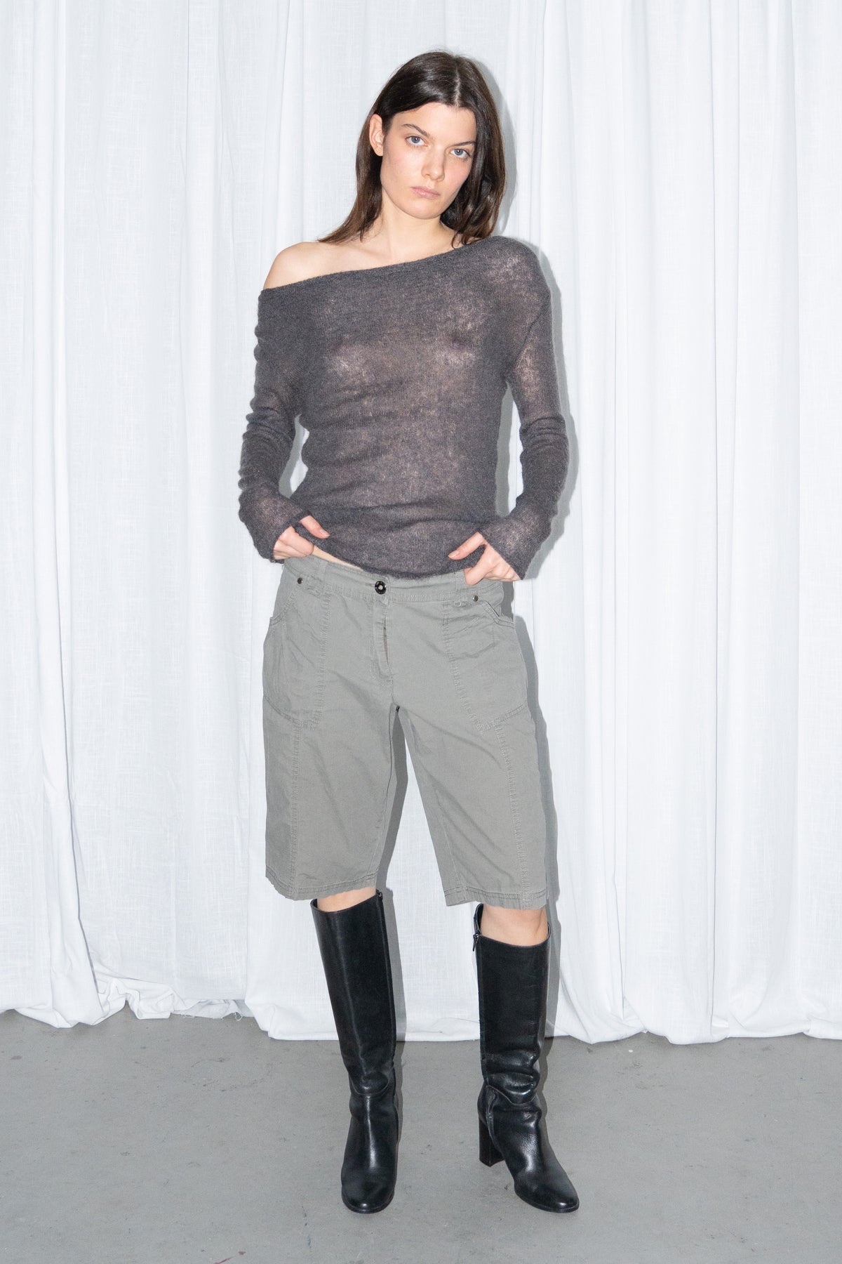Model posing in a charcoal brown off-shoulder fitted top with khaki green cargo Bermuda shorts and black knee boots