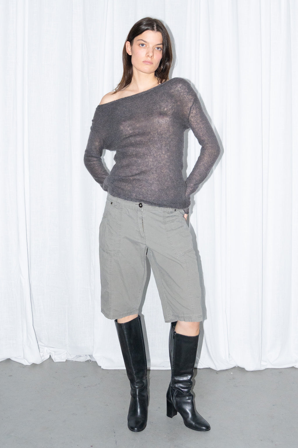 Model posing in a charcoal brown off-shoulder fitted top with khaki green cargo Bermuda shorts and black knee boots