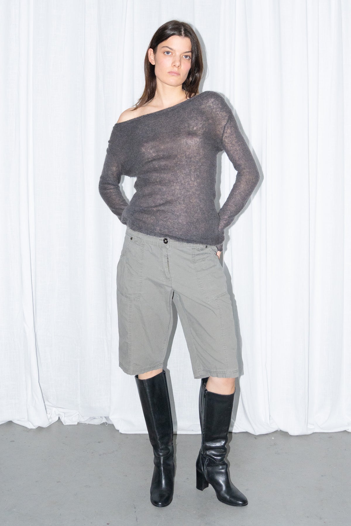 Model posing in a charcoal brown off-shoulder fitted top with khaki green cargo Bermuda shorts and black knee boots