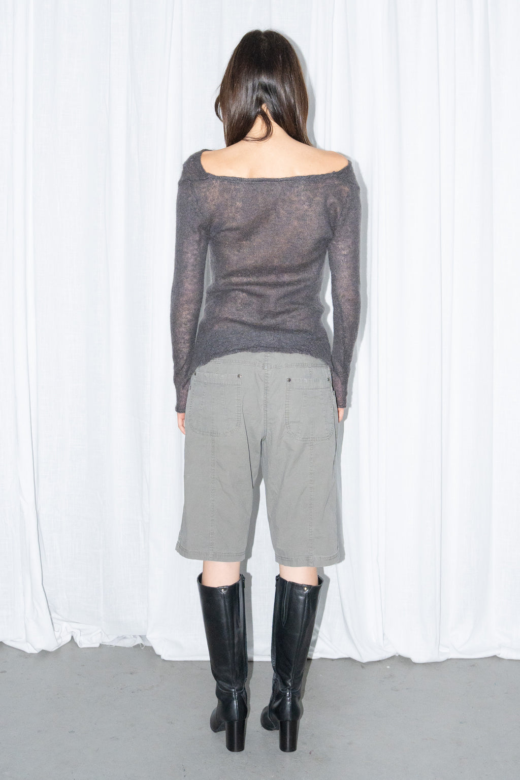 Back view of a charcoal brown off-shoulder fitted top with khaki green cargo Bermuda shorts and black knee boots