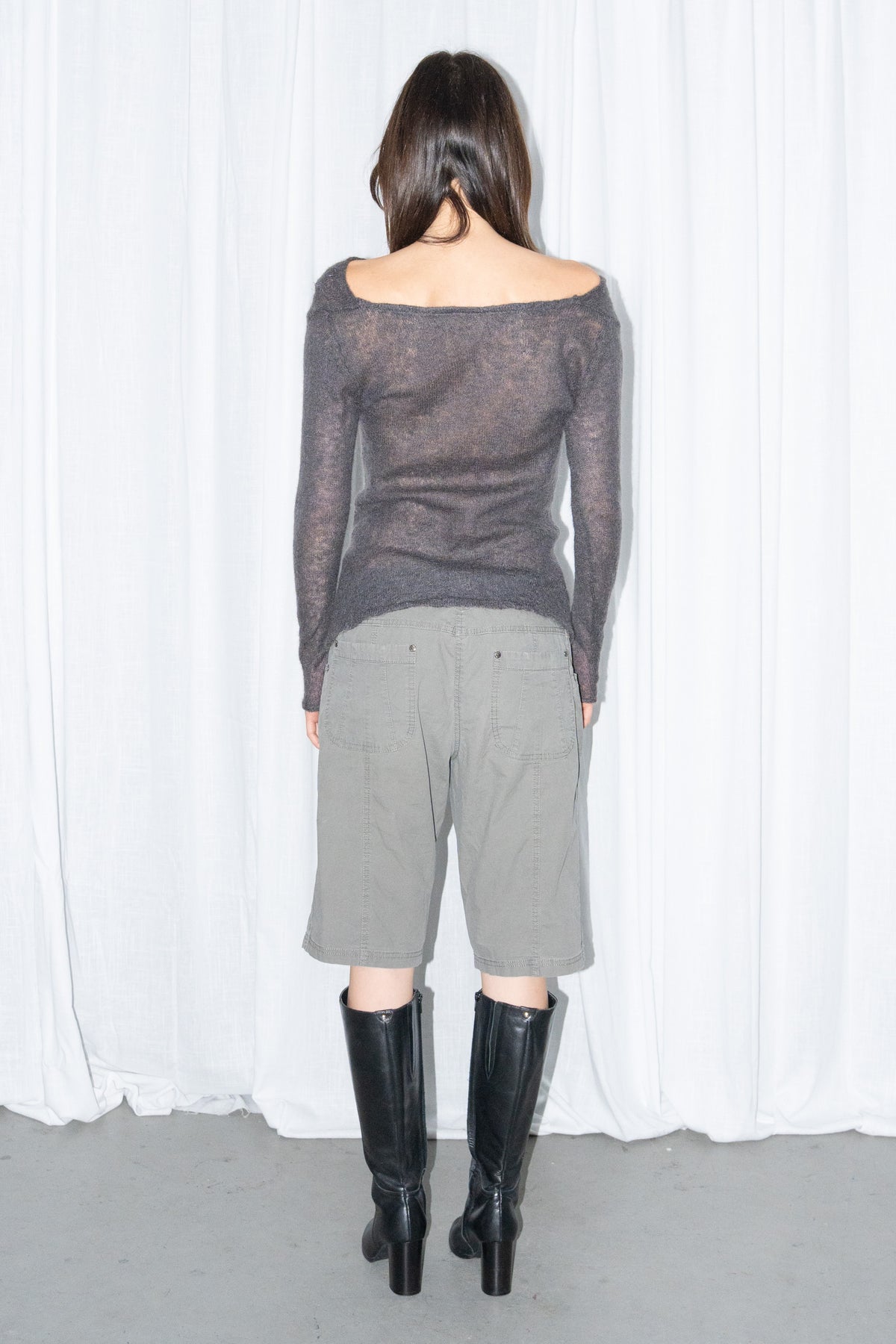 Back view of a charcoal brown off-shoulder fitted top with khaki green cargo Bermuda shorts and black knee boots