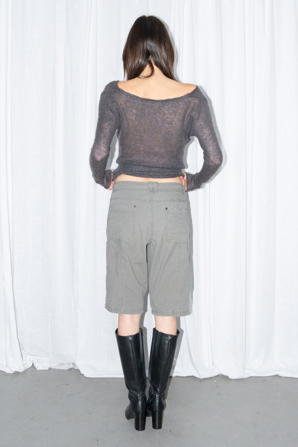 Back view of a charcoal brown off-shoulder fitted top with khaki green cargo Bermuda shorts and black knee boots