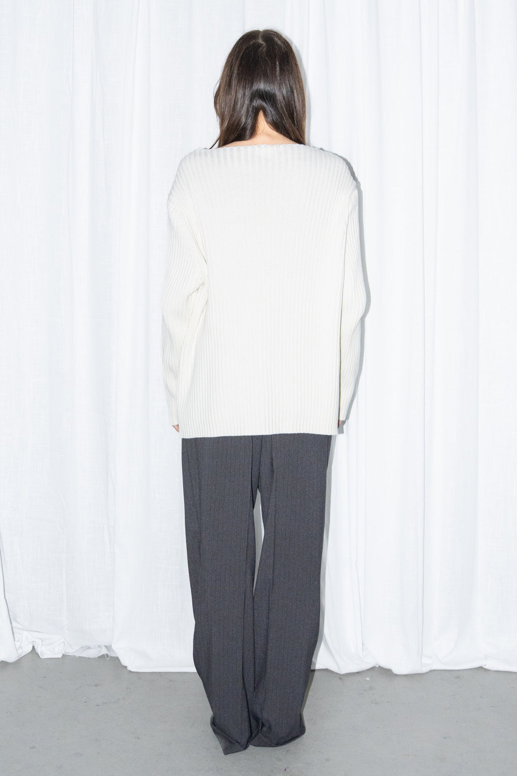 Back view of a cream ribbed knit long cardigan with black high-waist wide-leg trousers