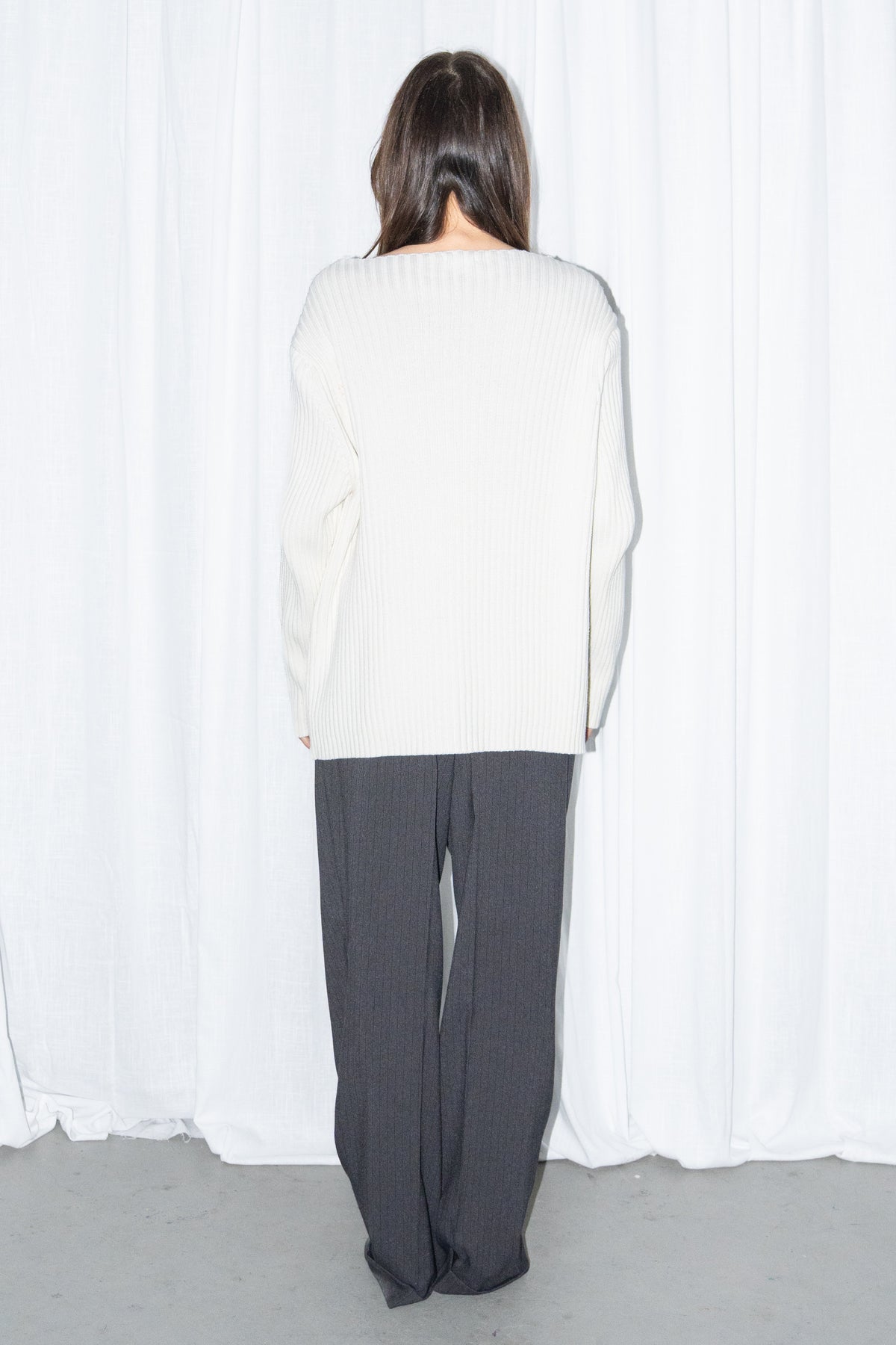 Back view of a cream ribbed knit long cardigan with black high-waist wide-leg trousers