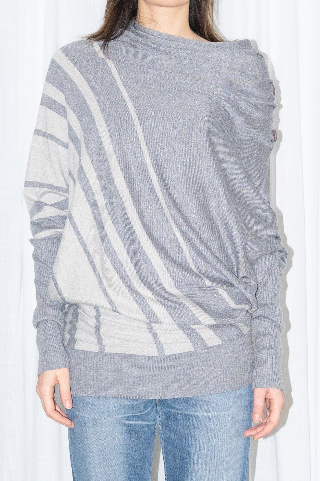 Close-up of a grey draped asymmetric knit top with light blue jeans