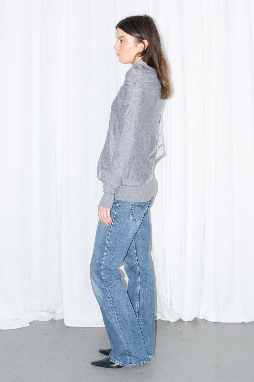 Model wearing a grey draped asymmetric knit top with light blue jeans