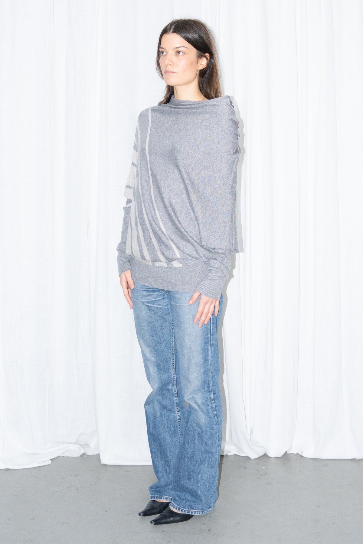 Model wearing a grey draped asymmetric knit top with light blue jeans