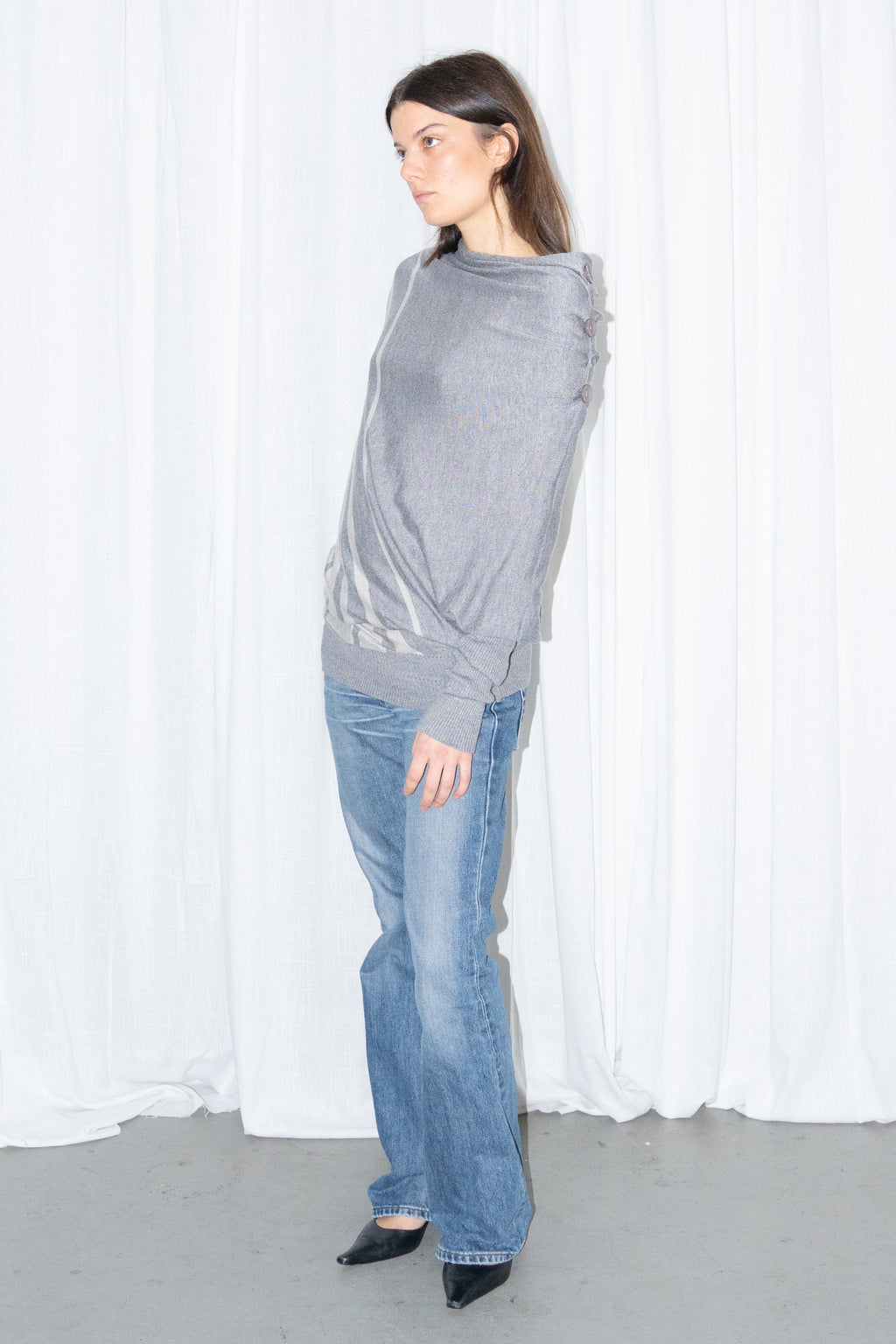 Model wearing a grey draped asymmetric knit top with light blue jeans