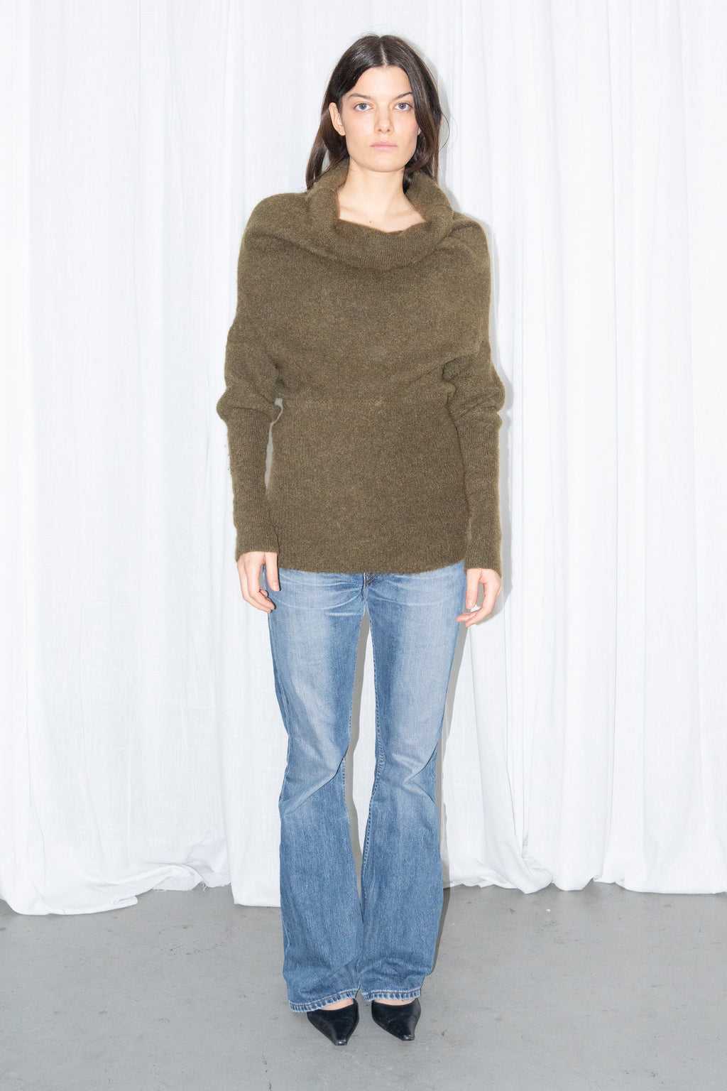 Model wearing an olive cowl-neck chunky knit sweater with light blue jeans