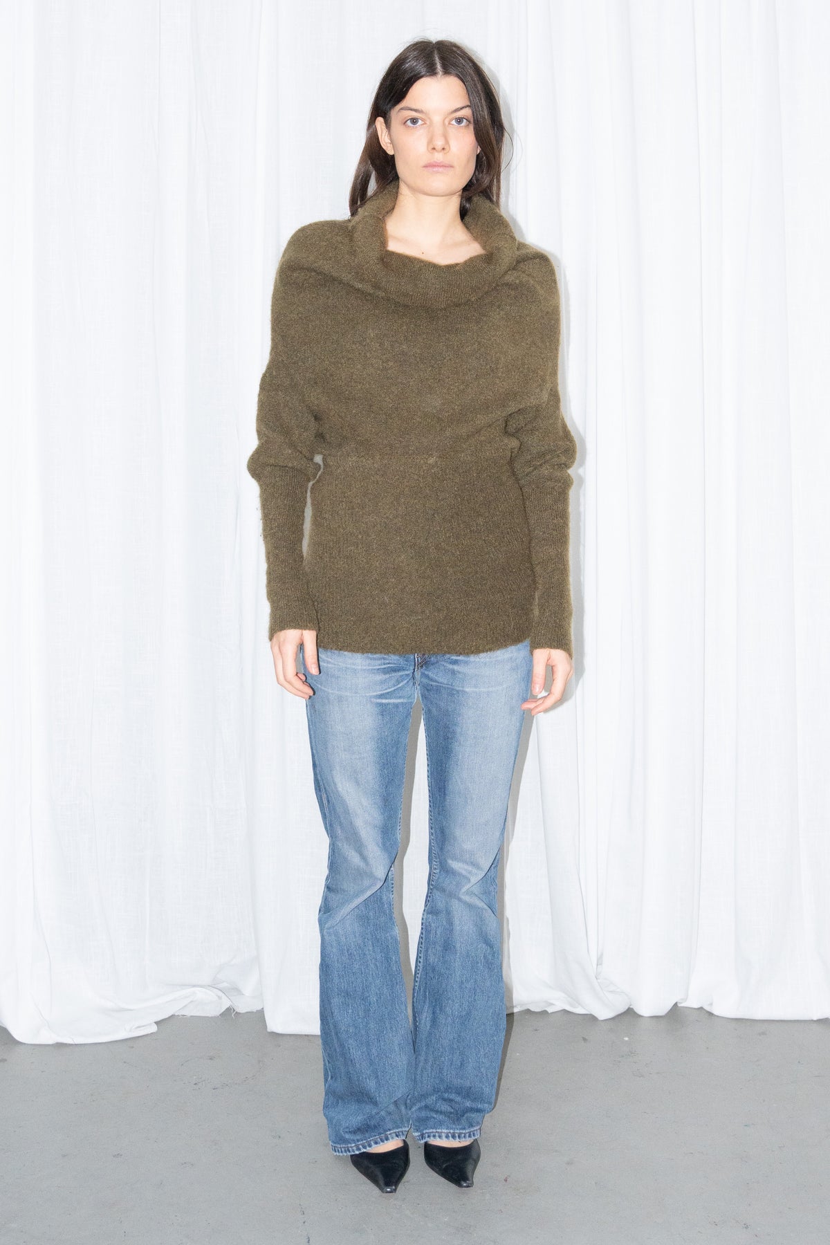Model wearing an olive cowl-neck chunky knit sweater with light blue jeans