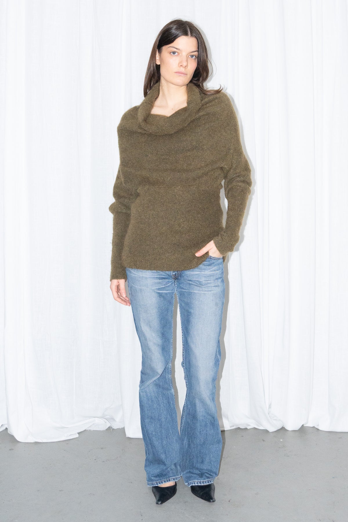 Model wearing an olive cowl-neck chunky knit sweater with light blue jeans