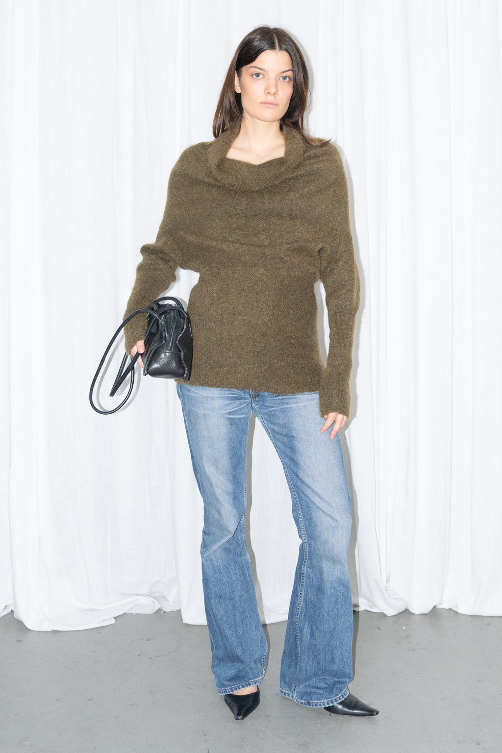 Model wearing an olive cowl-neck chunky knit sweater with light blue jeans