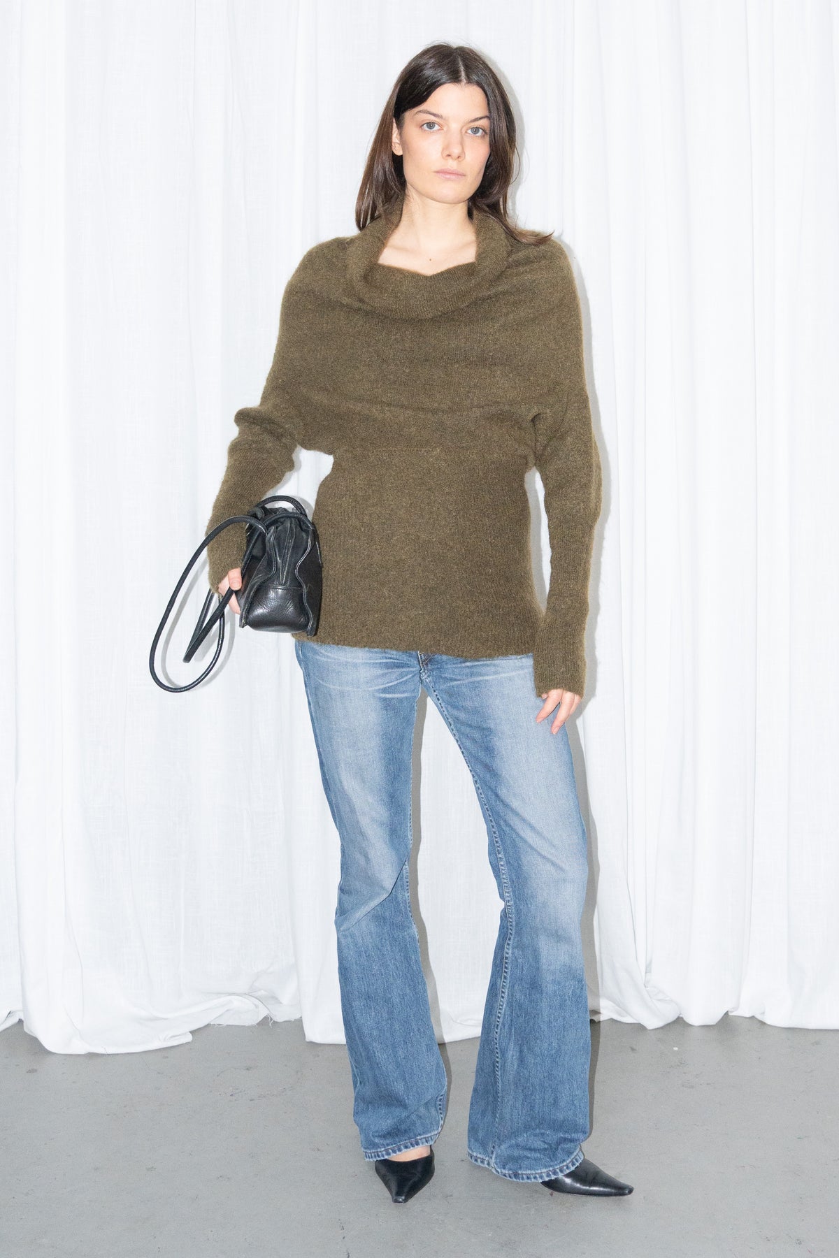 Model wearing an olive cowl-neck chunky knit sweater with light blue jeans