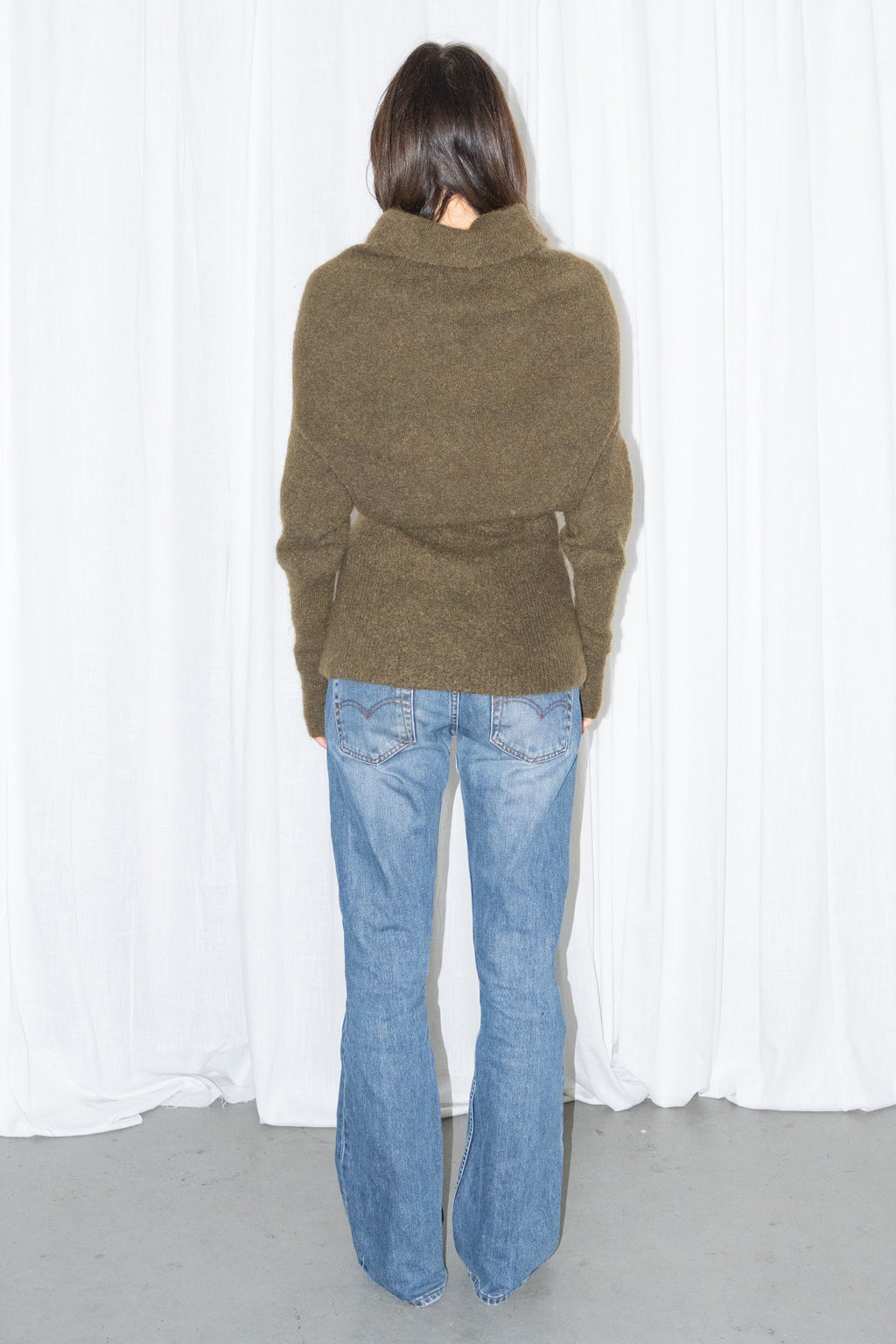 Back view of an olive cowl-neck chunky knit sweater with light blue jeans