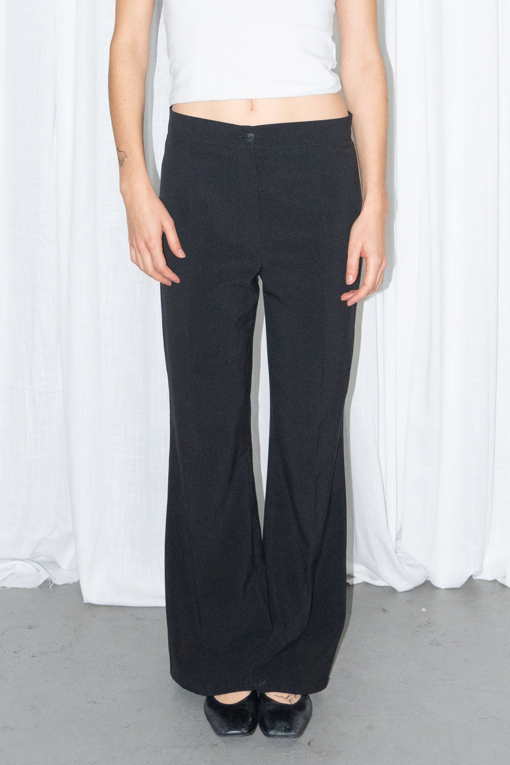 Close-up of black low-rise trousers worn with a white fitted T-shirt