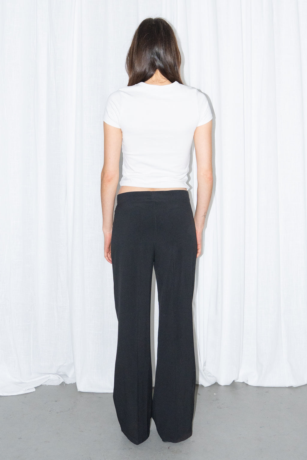 Back view of a white fitted T-shirt with black low-rise trousers