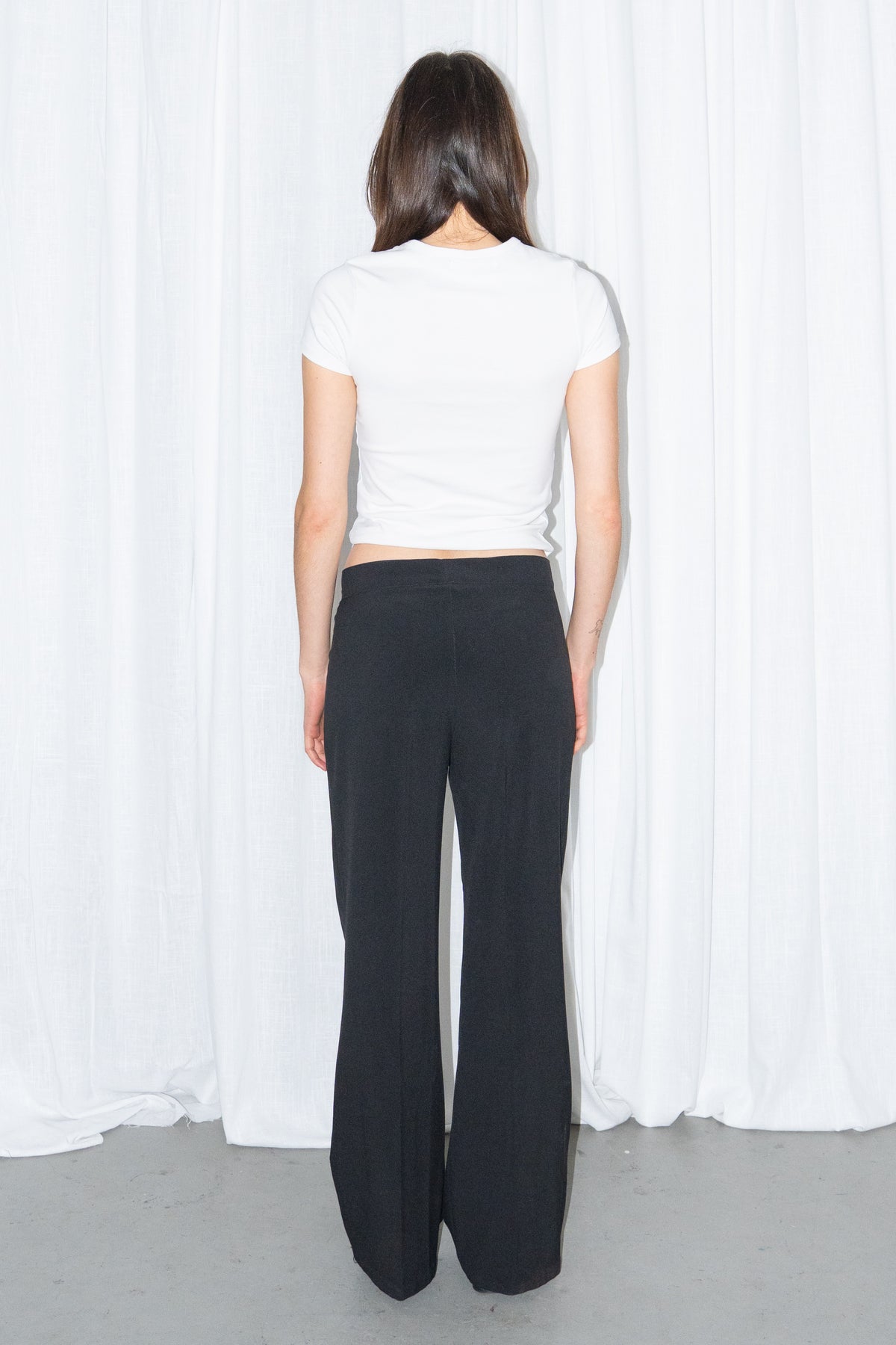 Back view of a white fitted T-shirt with black low-rise trousers