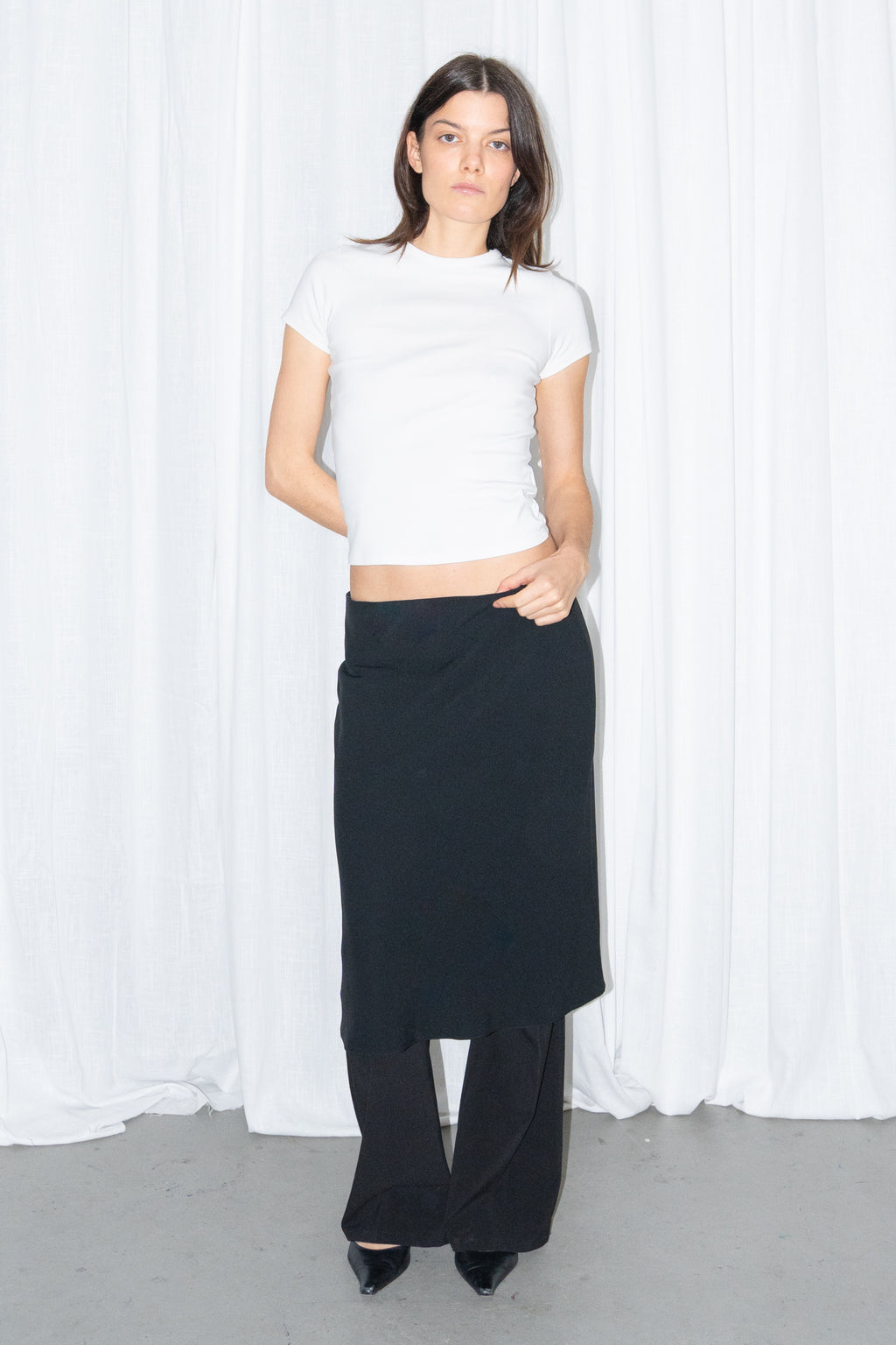 Model wearing a white fitted T-shirt with a black flared midi skirt over black trousers