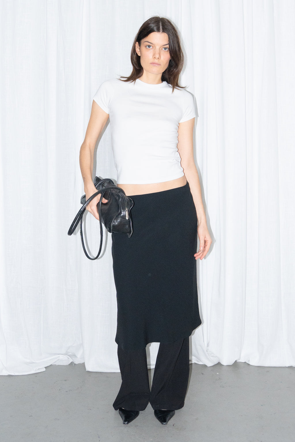 Model wearing a white fitted T-shirt with a black flared midi skirt over black trousers