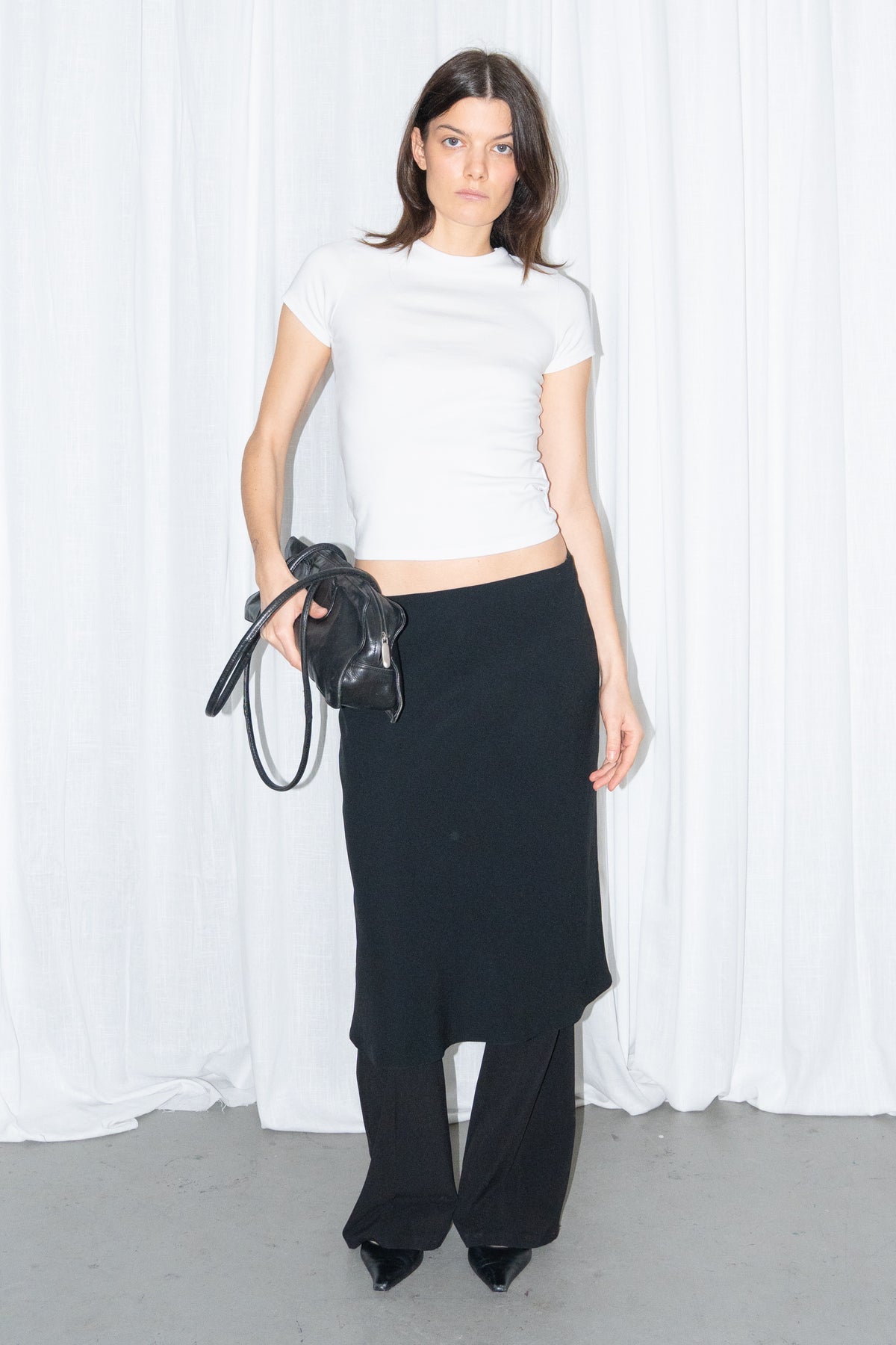 Model wearing a white fitted T-shirt with a black flared midi skirt over black trousers