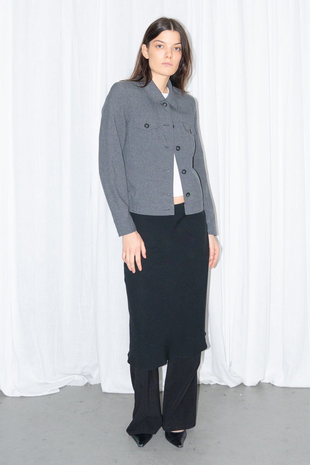 Model wearing a grey 5-pocket blazer jacket with a white T-shirt and a black flared midi skirt over black trousers