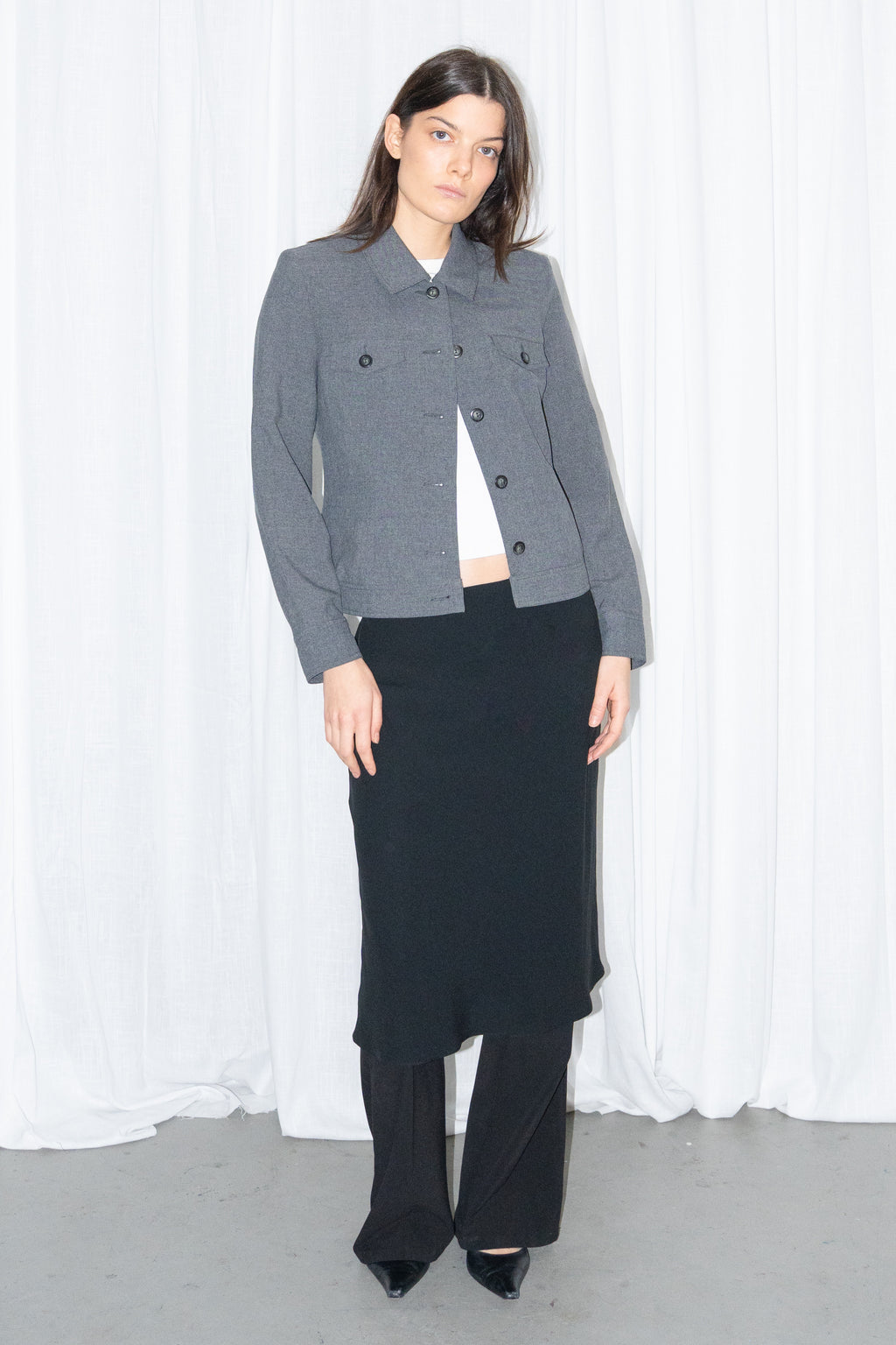 Model wearing a grey 5-pocket blazer jacket with a white T-shirt and a black flared midi skirt over black trousers