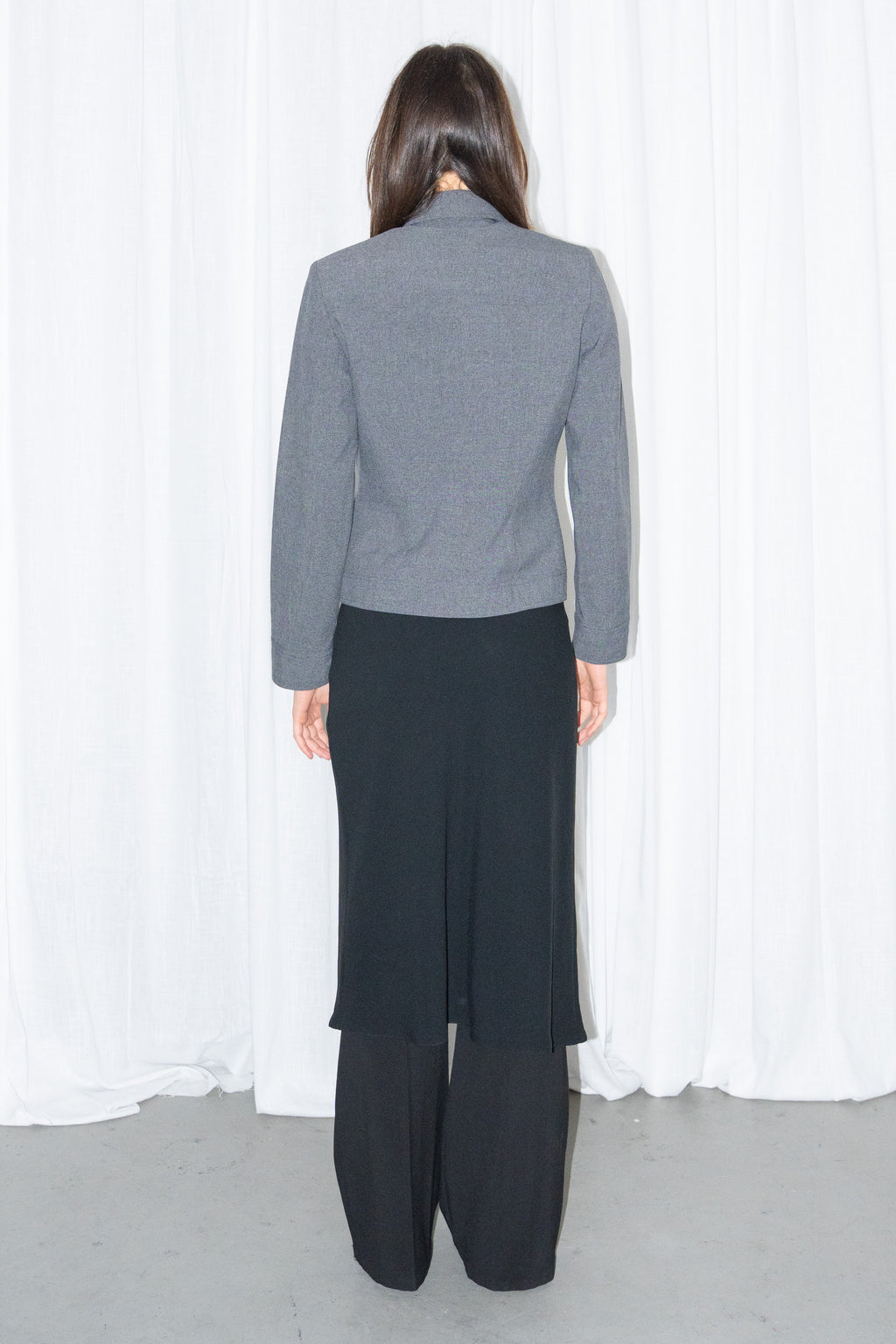 Back view of a grey 5-pocket blazer jacket with a white T-shirt and a black flared midi skirt over black trousers