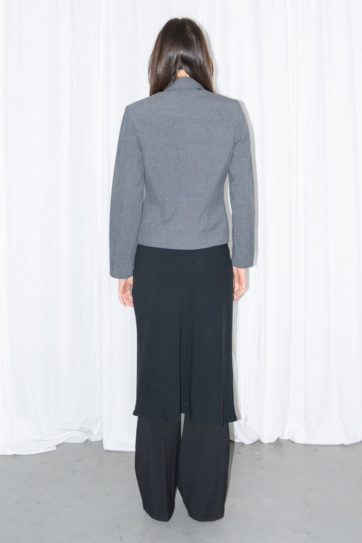 Back view of a grey 5-pocket blazer jacket with a white T-shirt and a black flared midi skirt over black trousers