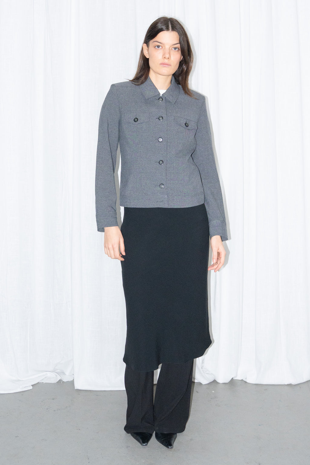 Model wearing a grey 5-pocket blazer jacket with a white T-shirt and a black flared midi skirt over black trousers