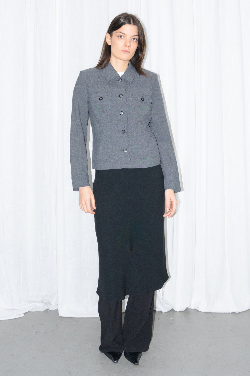 Model wearing a grey 5-pocket blazer jacket with a white T-shirt and a black flared midi skirt over black trousers