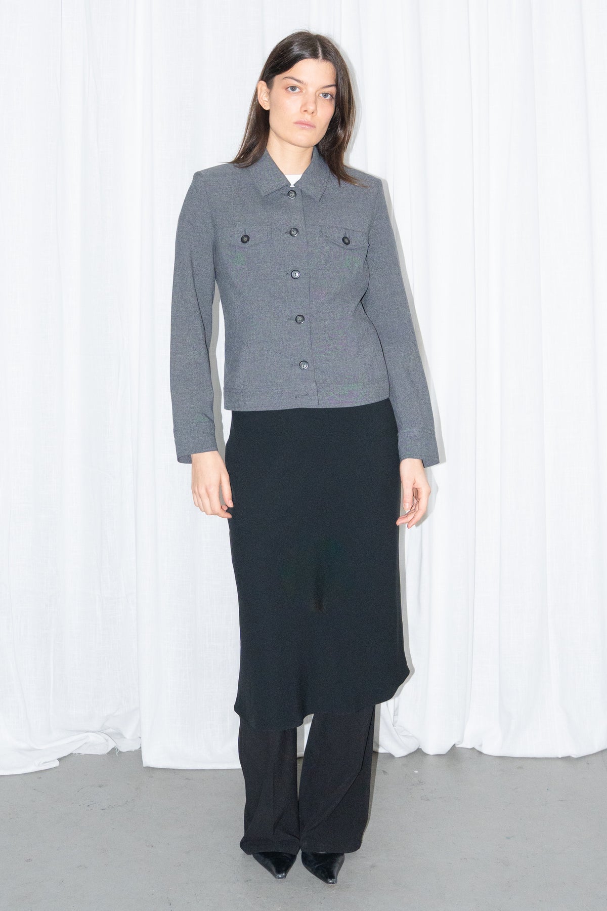 Model wearing a grey 5-pocket blazer jacket with a white T-shirt and a black flared midi skirt over black trousers