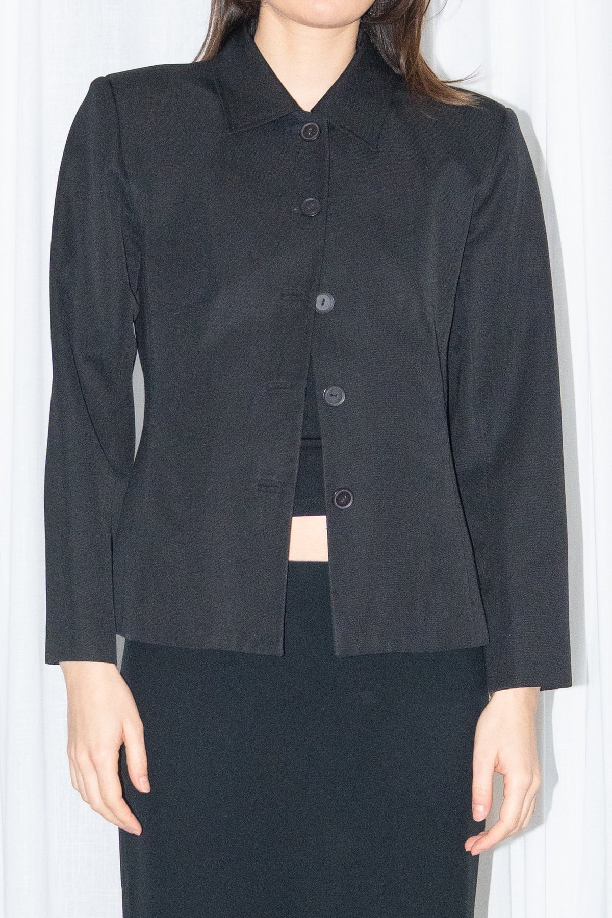Close-up of black boxy button-up jacket with a black flared midi skirt over black trousers – MINIFALDA