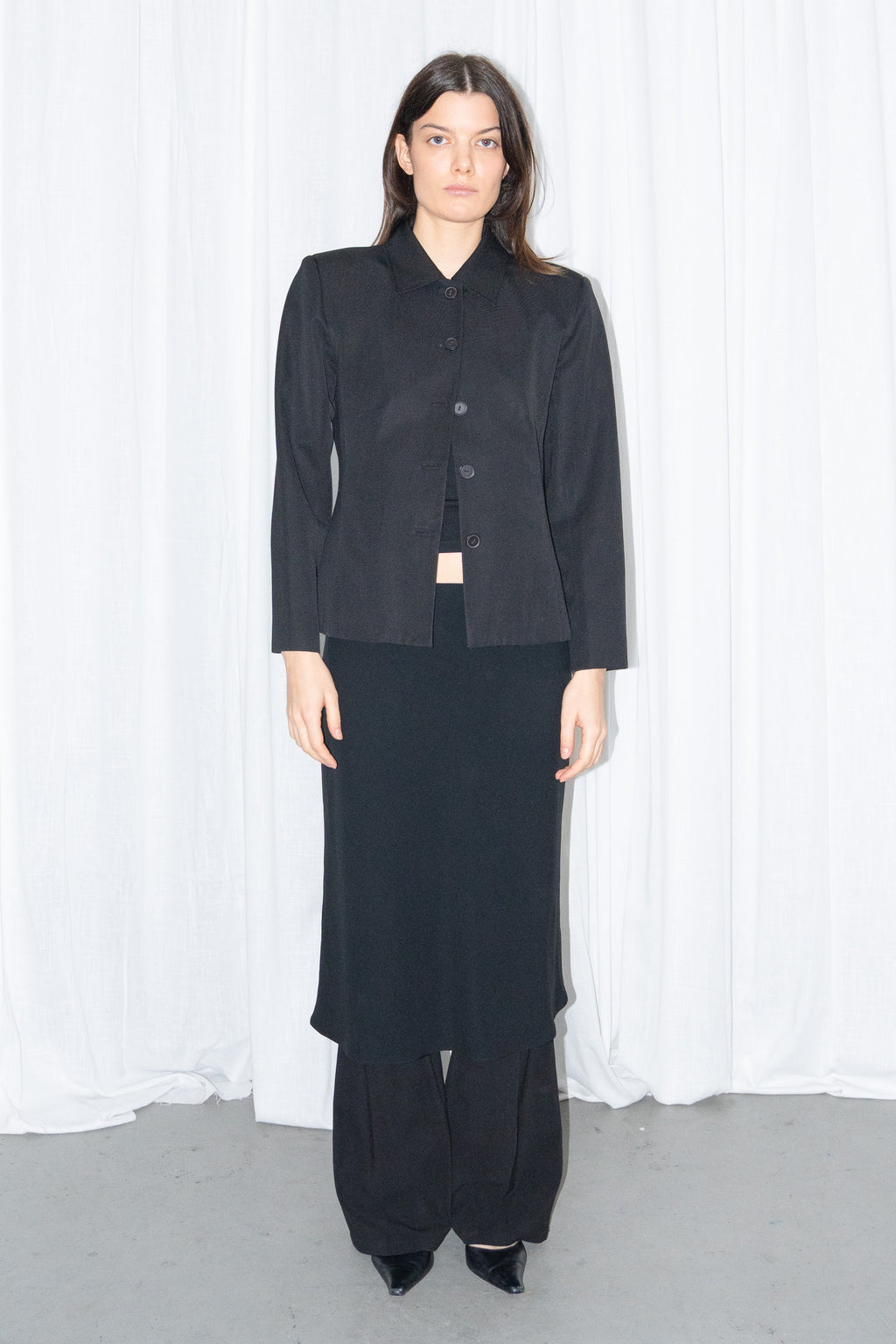 Model wearing black boxy button-up jacket with a black flared midi skirt over black trousers – MINIFALDA