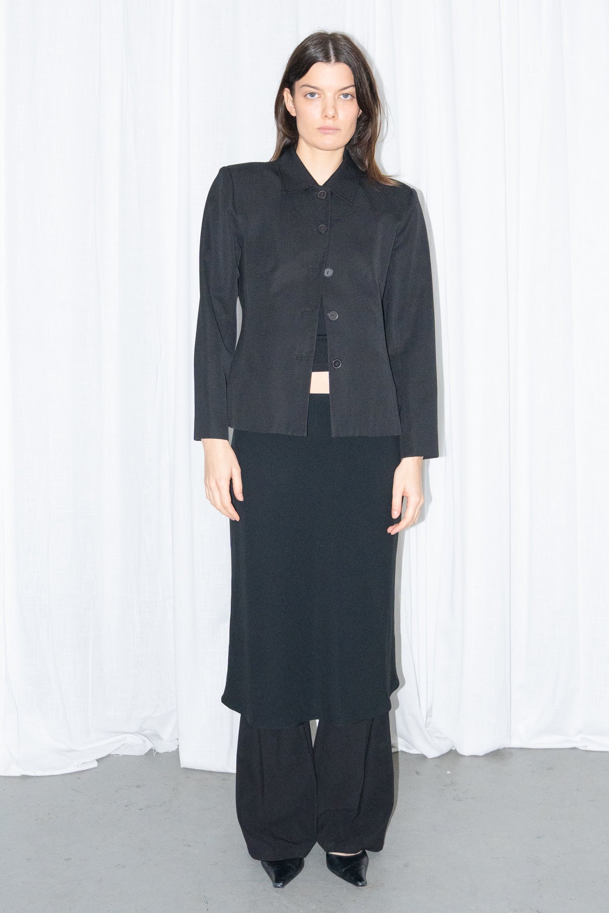 Model wearing black boxy button-up jacket with a black flared midi skirt over black trousers – MINIFALDA