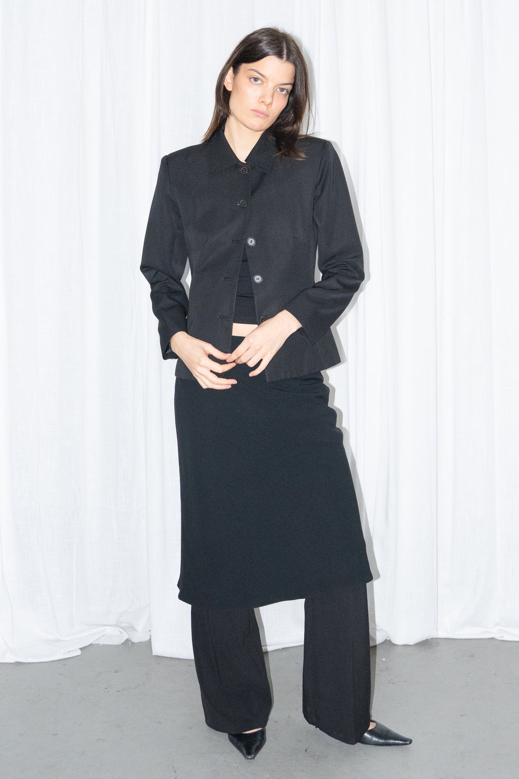 Model wearing black boxy button-up jacket with a black flared midi skirt over black trousers – MINIFALDA