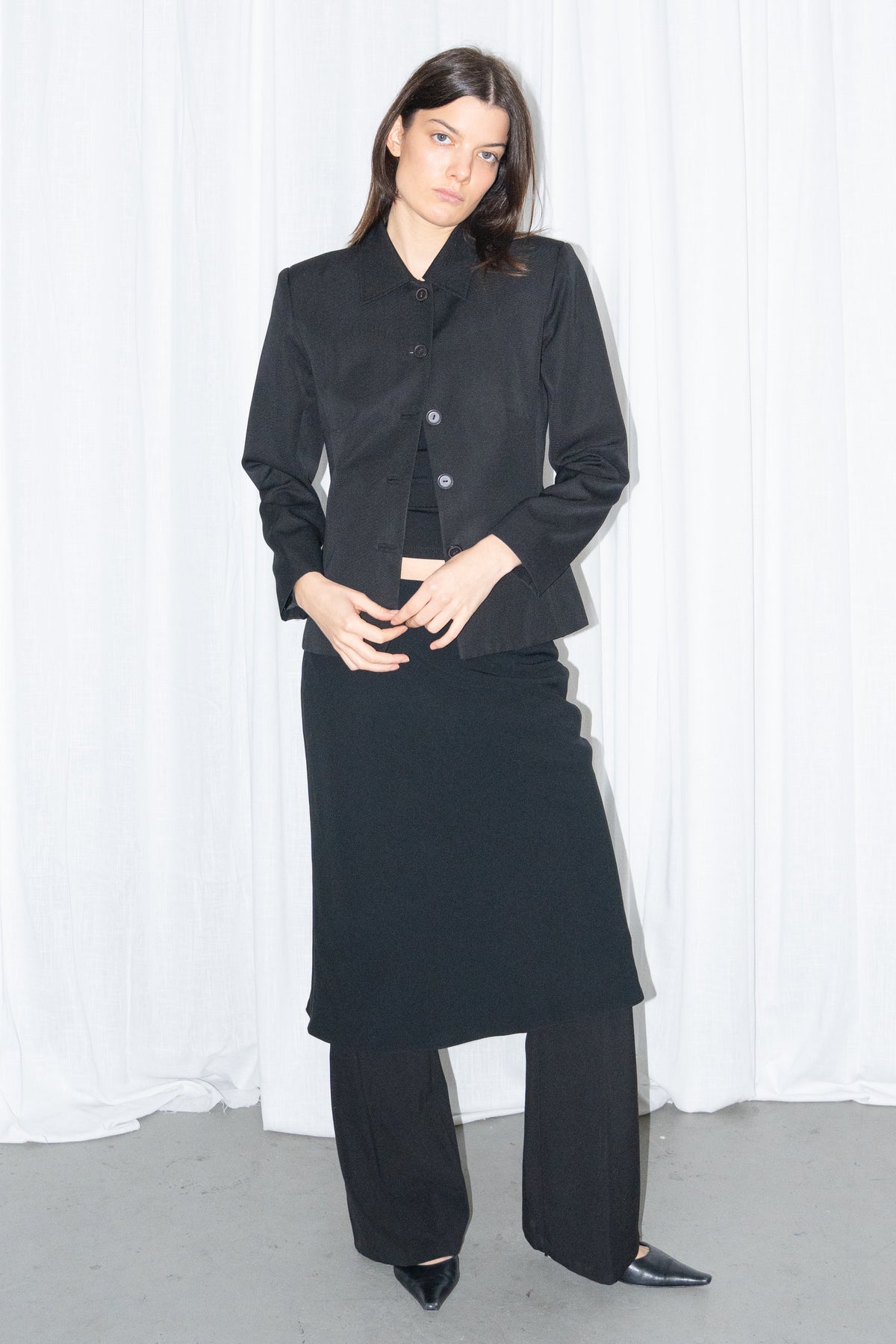 Model wearing black boxy button-up jacket with a black flared midi skirt over black trousers – MINIFALDA