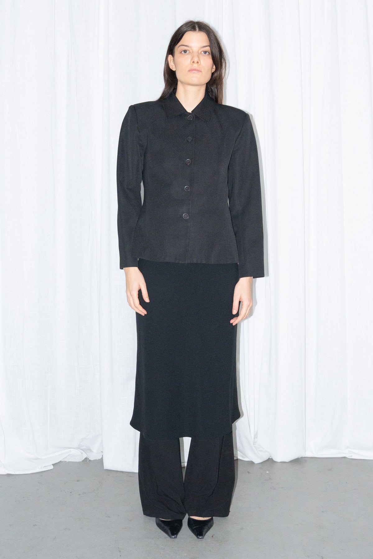 Model wearing black boxy button-up jacket with a black flared midi skirt over black trousers – MINIFALDA