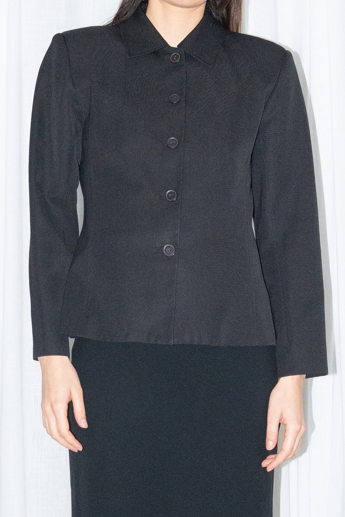 Close-up of black boxy button-up jacket with a black flared midi skirt over black trousers – MINIFALDA