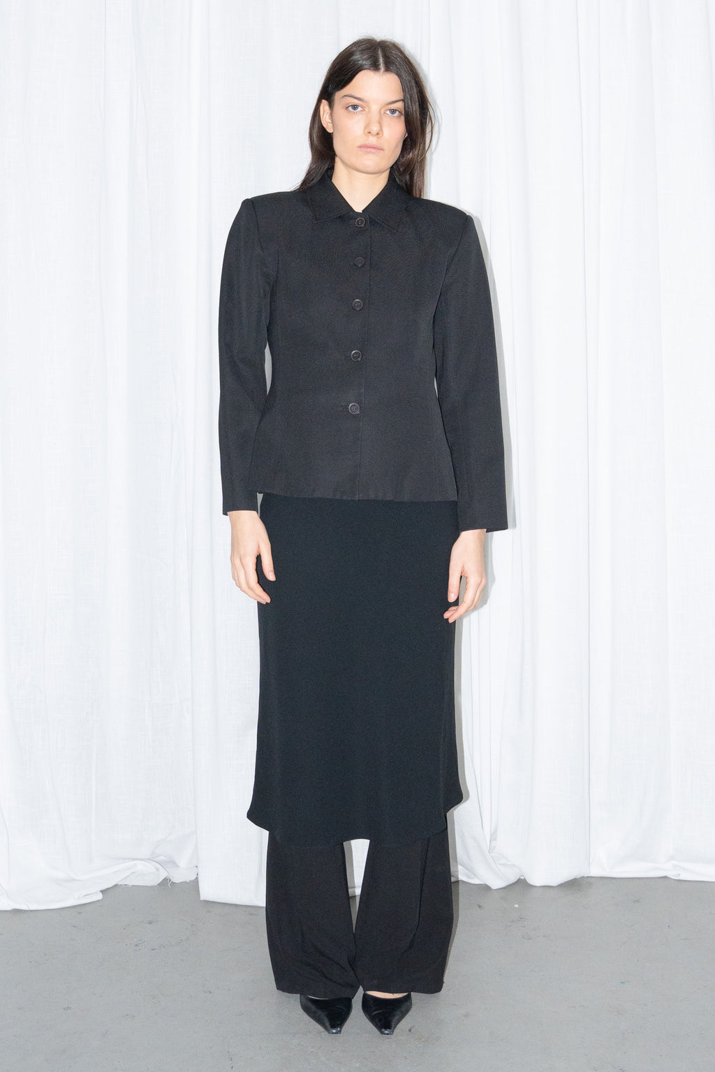 Model wearing black boxy button-up jacket with a black flared midi skirt over black trousers – MINIFALDA