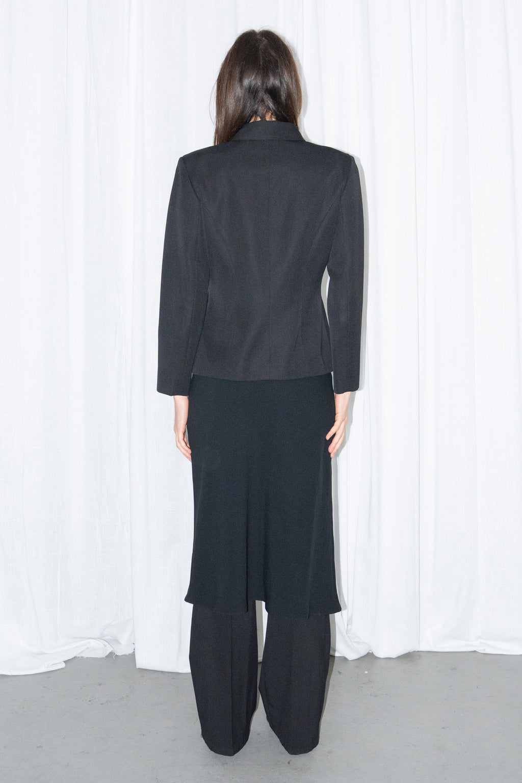 Model wearing black boxy button-up jacket with a black flared midi skirt over black trousers – MINIFALDA